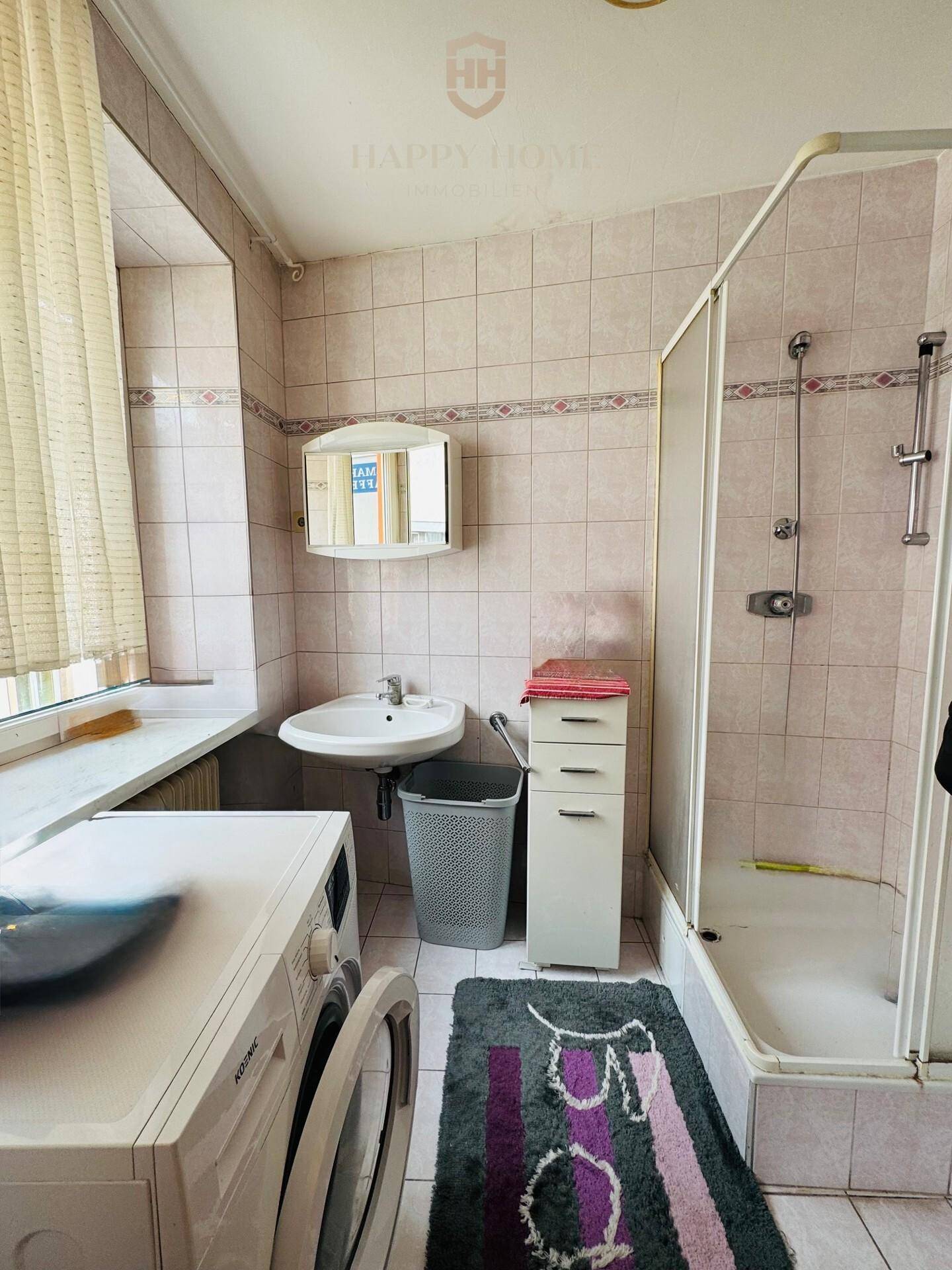 Badezimmer mit Dusche, Waschmaschine, Waschbecken und hellen Fliesen.