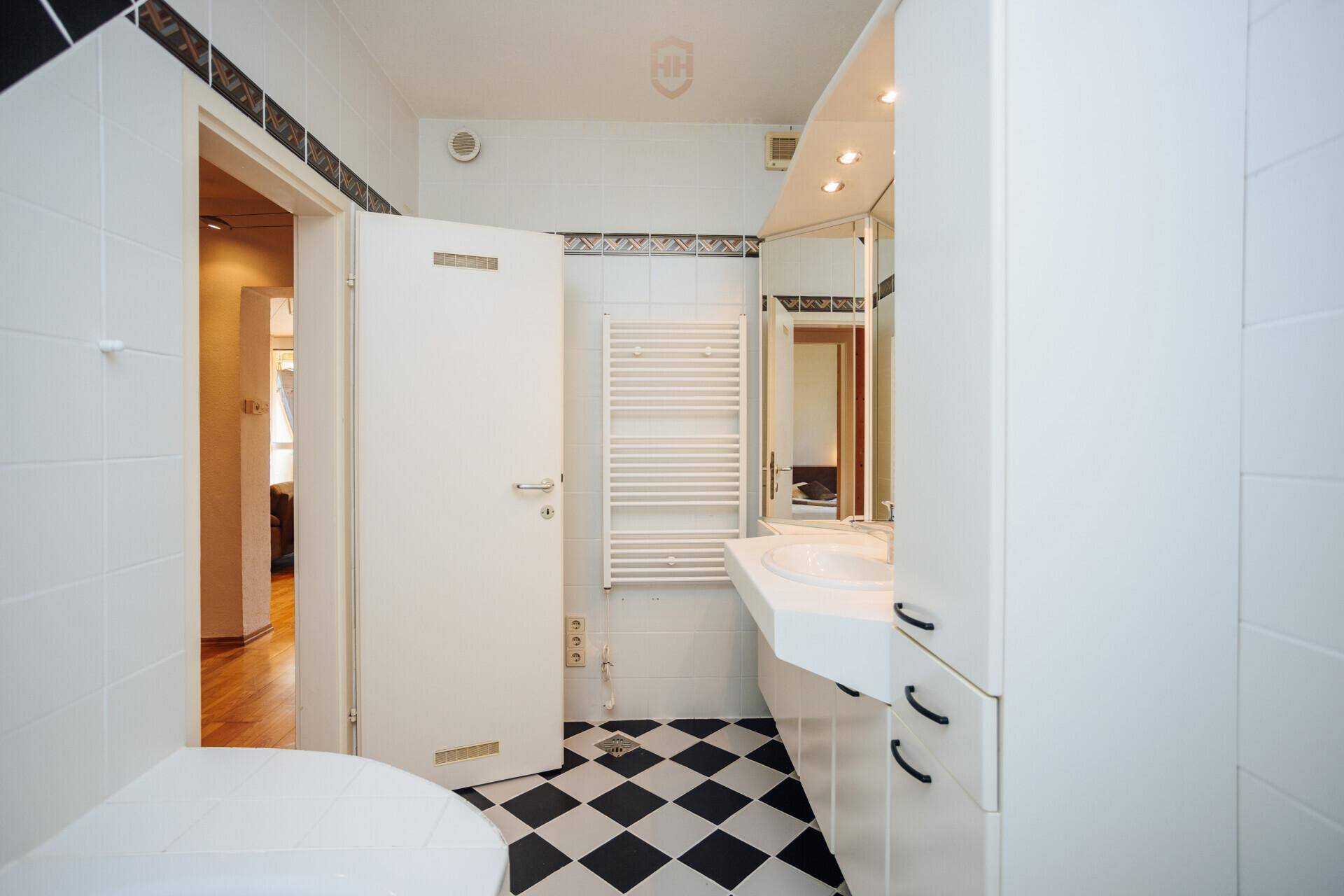 Badezimmer mit schwarz-weiß kariertem Fliesenboden, Waschtisch und Spiegelschrank.