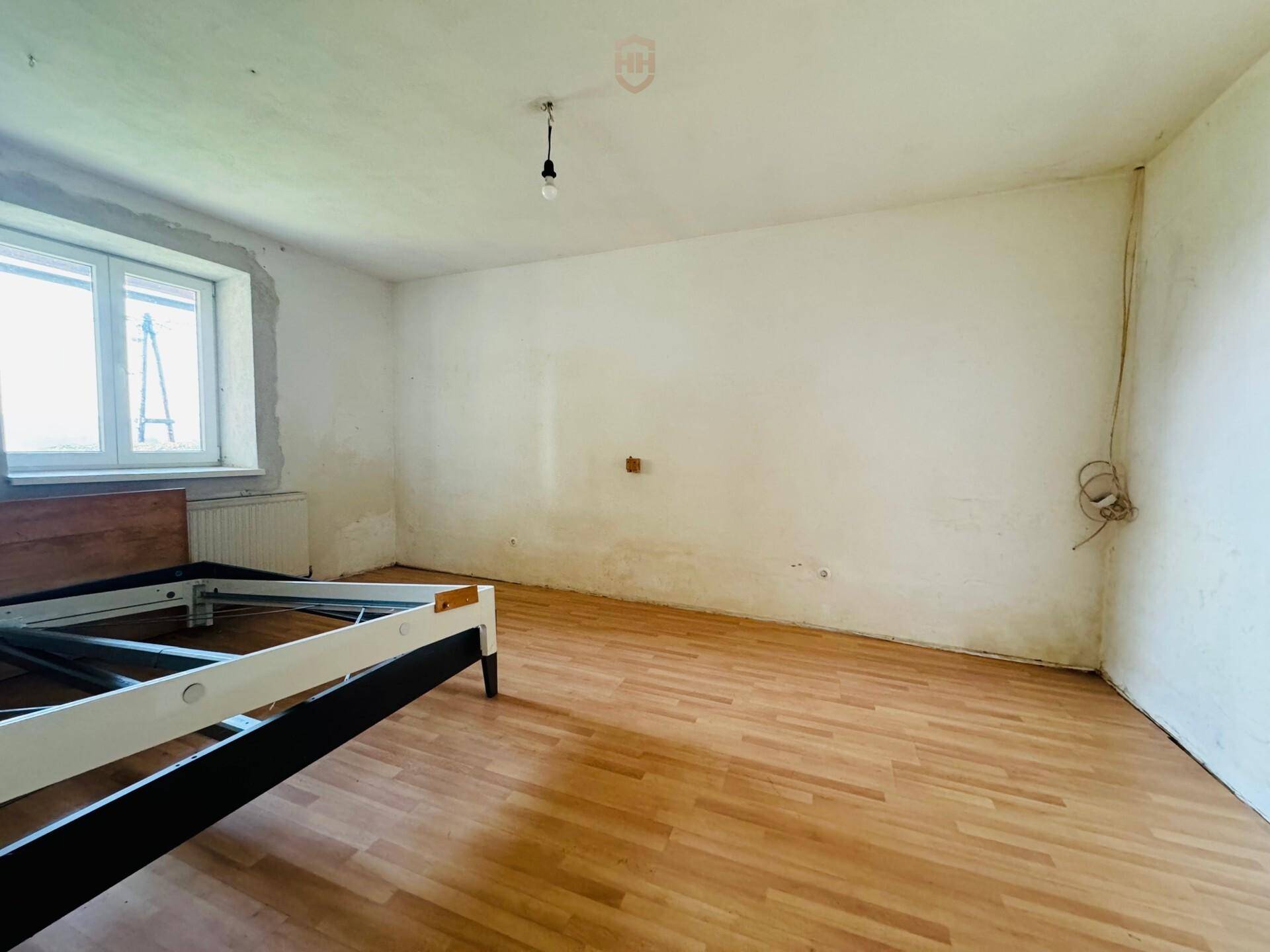 Schlafzimmer mit Laminatboden und Fenster, das auf die grüne Umgebung blickt.