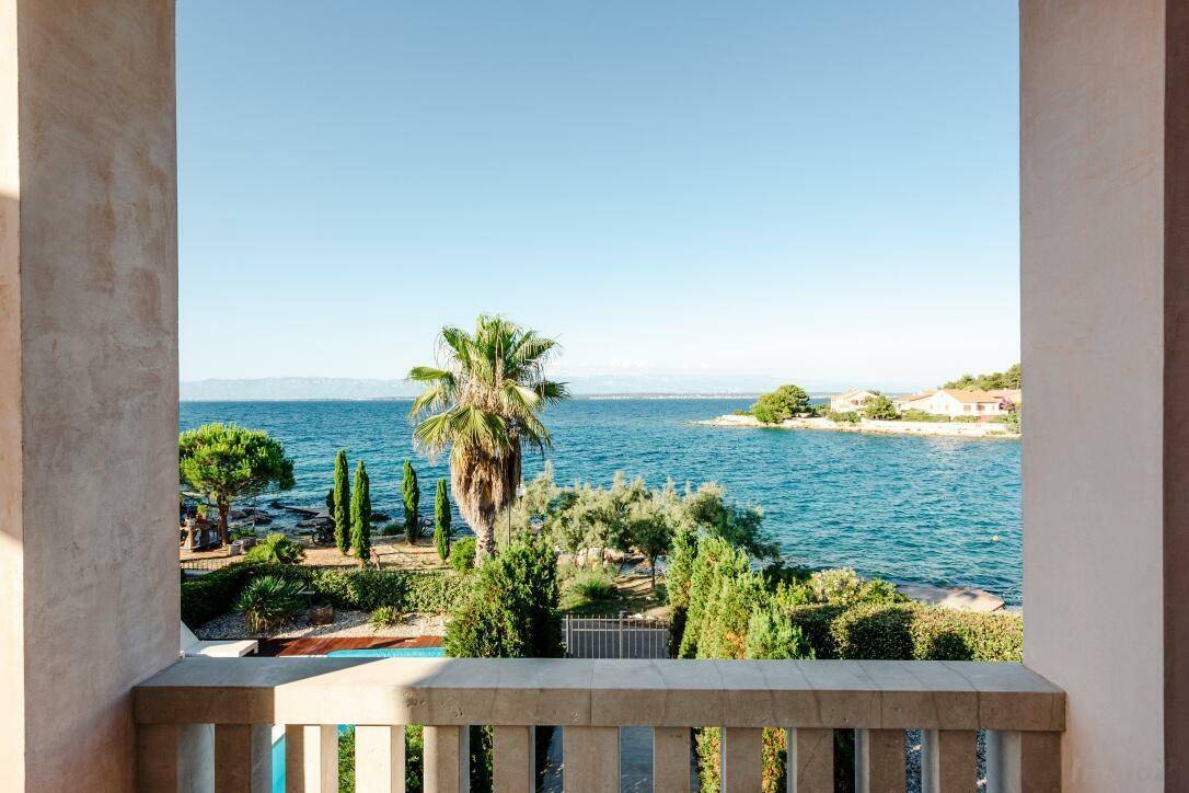 Atemberaubender Meerblick von einem Balkon mit Steinbrüstung, umgeben von mediterraner Vegetation.