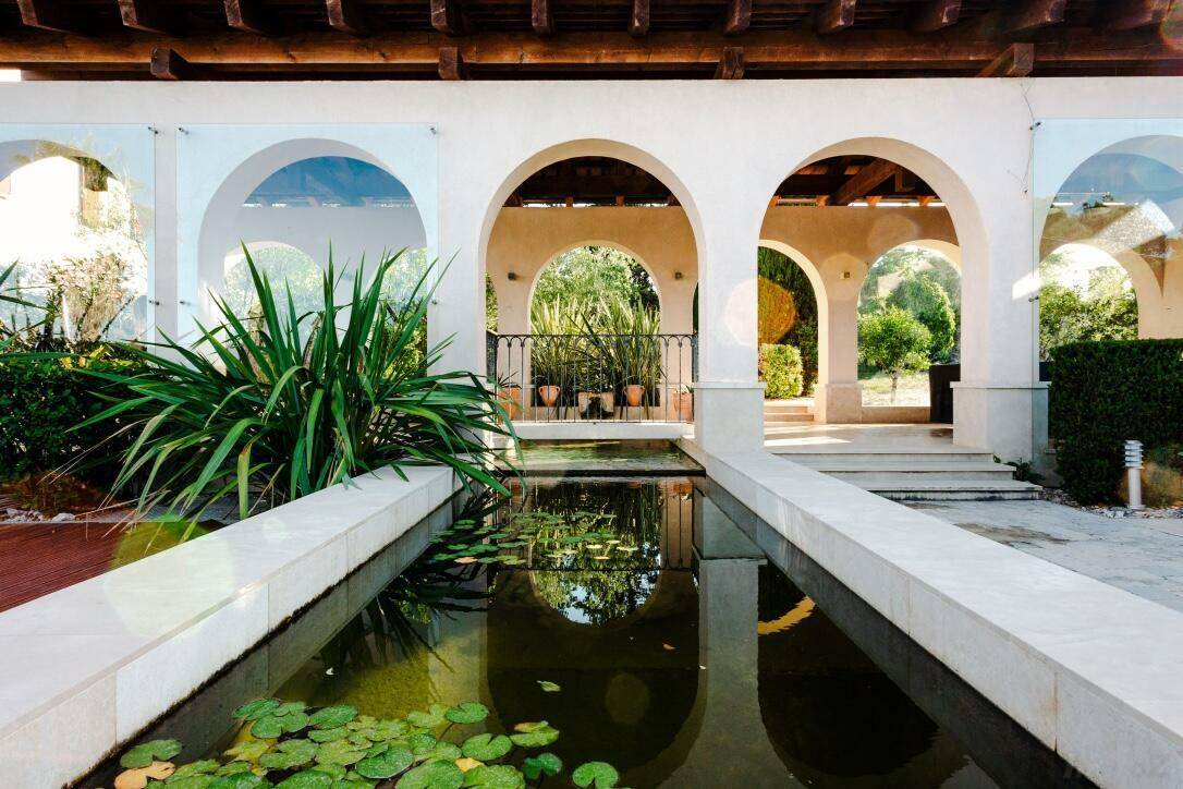 Ruhiger Gartenbereich mit einem langen Wasserbecken, Seerosen und eleganten Arkaden im mediterranen Stil.