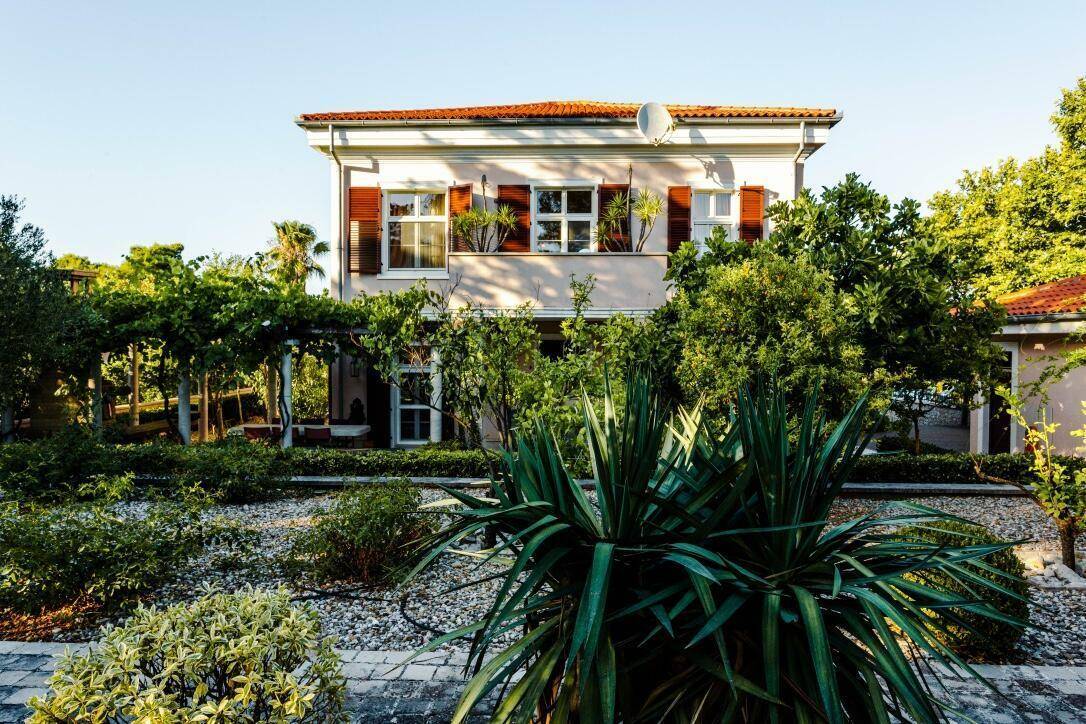 Villa eingebettet in einen üppigen mediterranen Garten mit verschiedenen Pflanzen und Kieswegen.
