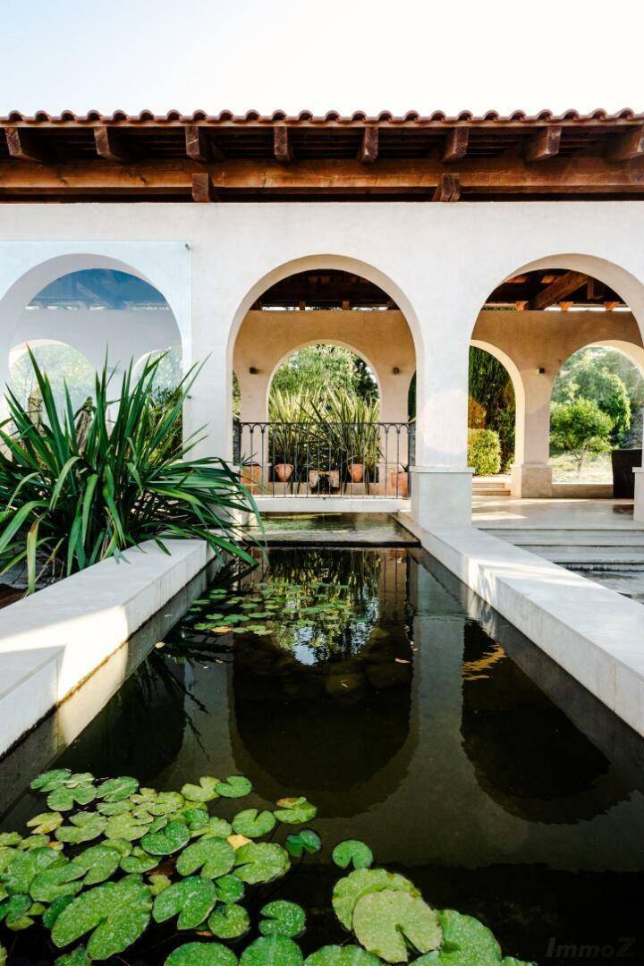 Mediterraner Gartenbereich mit einem langen Wasserbecken, Seerosen und eleganten Arkaden.