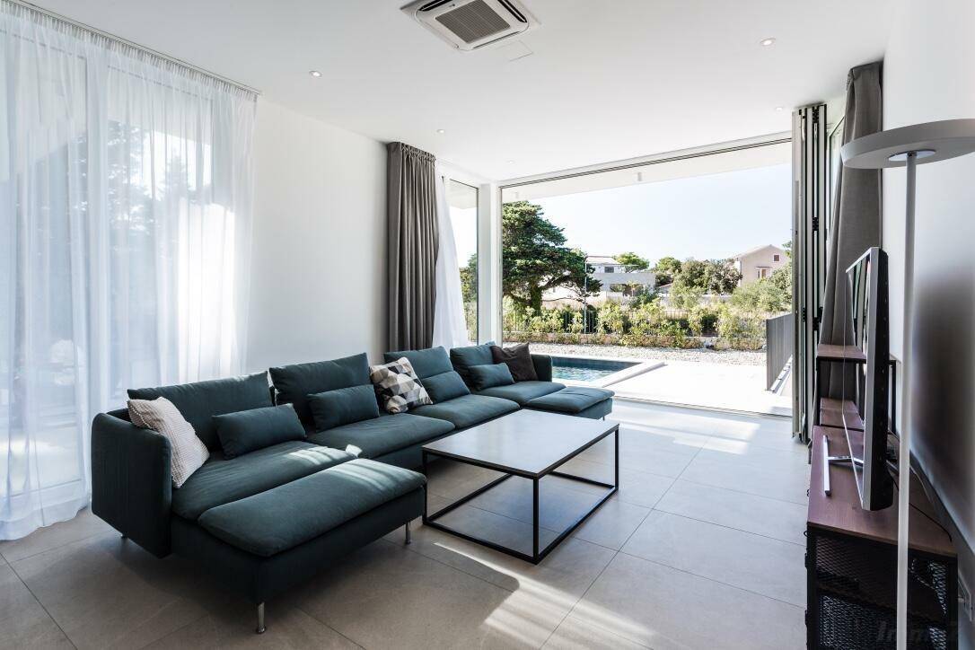 Lichtdurchflutetes Wohnzimmer mit moderner Einrichtung, großem Sofa und Blick auf den Poolbereich.