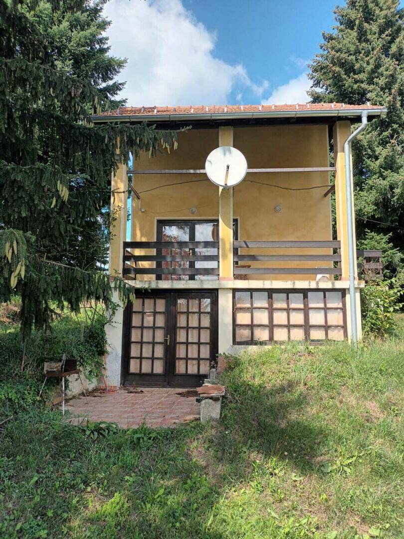 Vorderansicht des gelben Hauses mit Balkon im Obergeschoss und Zugang zum Gartenbereich.