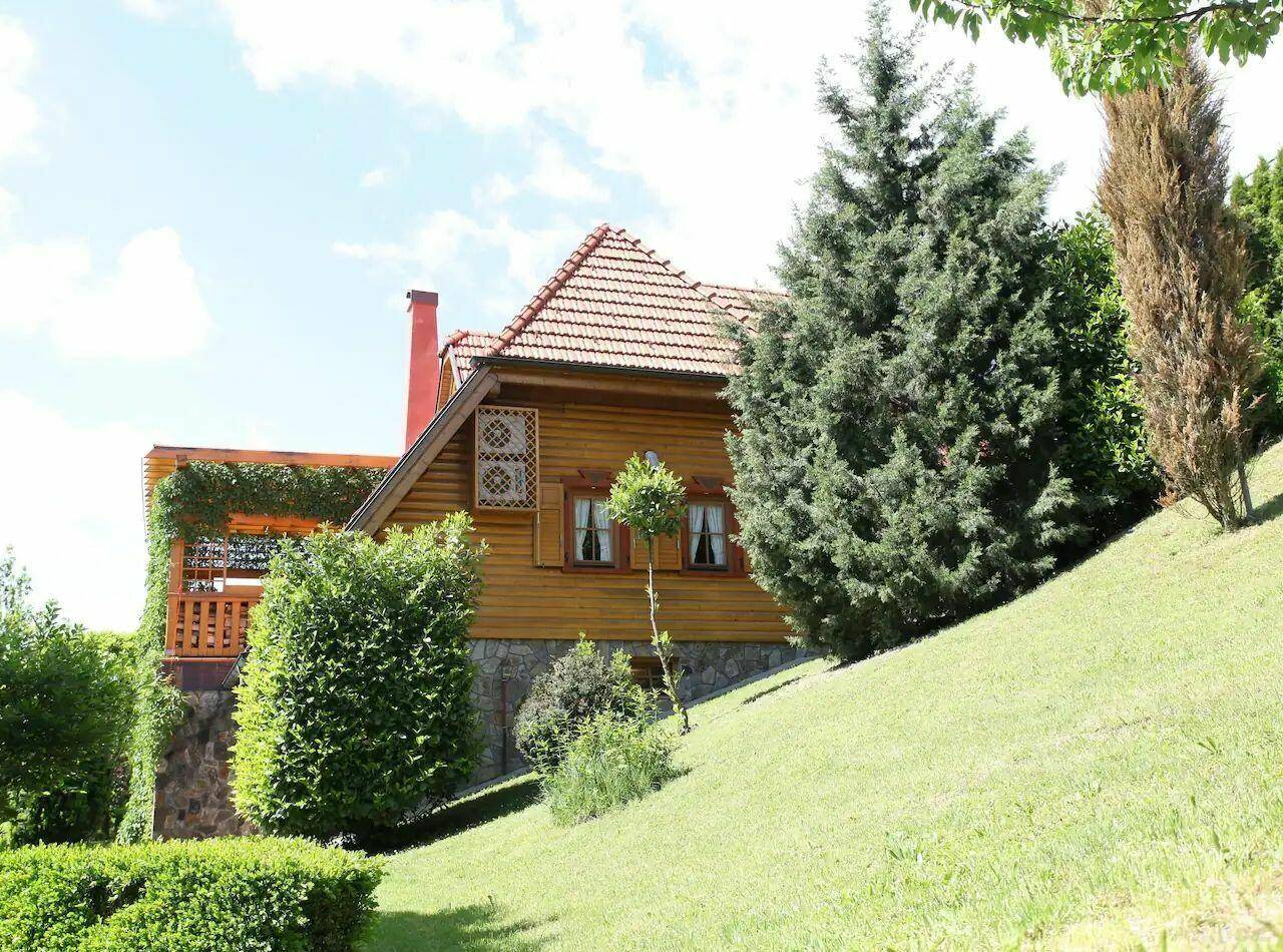 Holzhaus auf einem Hanggrundstück mit üppiger Bepflanzung und gepflegtem Rasen.