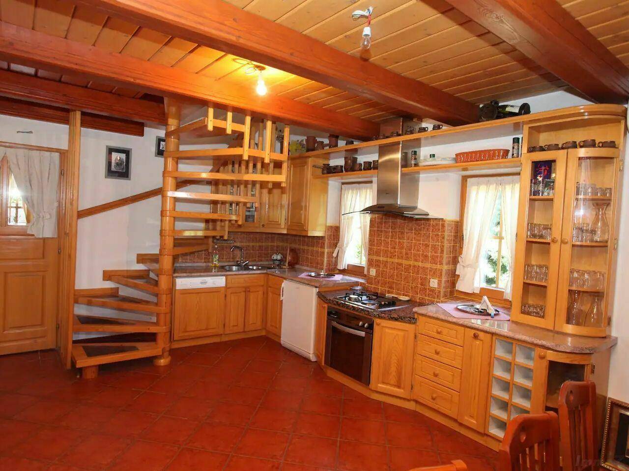 Rustikale Holzküche mit Wendeltreppe, Gasherd und Terrakotta-Fliesenboden.