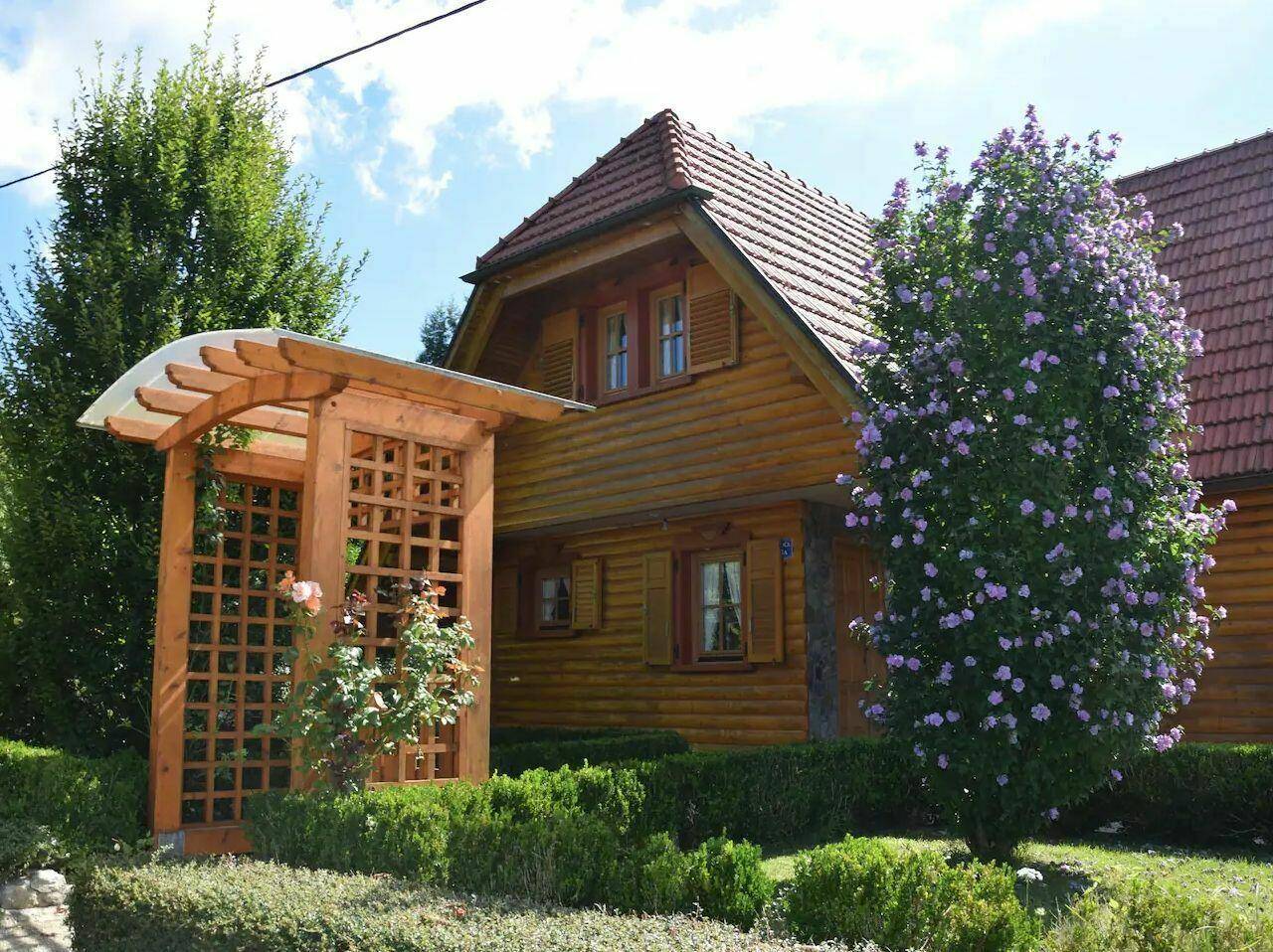 Holzhaus mit gepflegtem Vorgarten, blühenden Sträuchern und einem dekorativen Holzbogen.