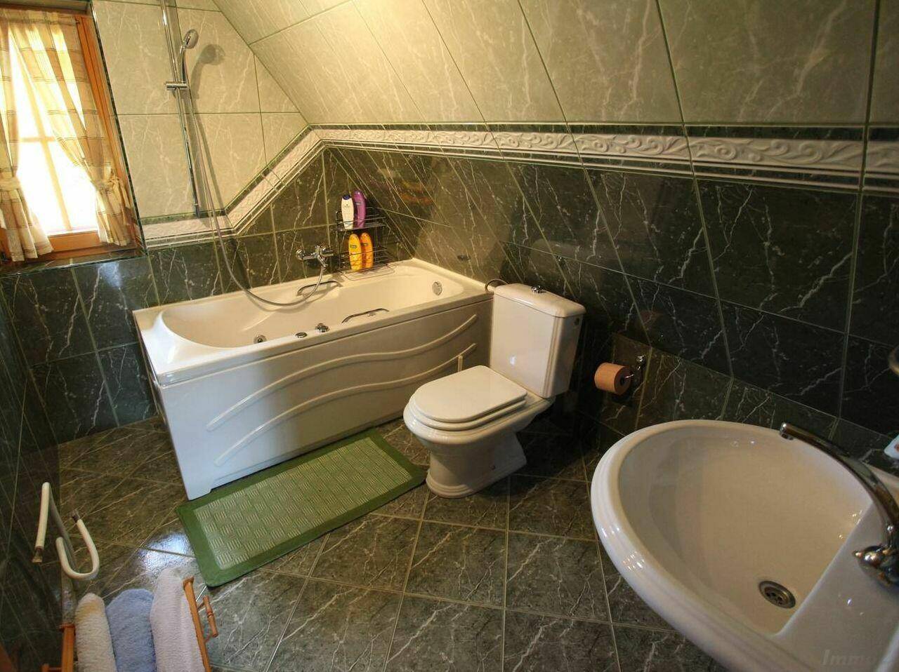 Badezimmer mit Badewanne, WC, Bidet und dunkelgrünen Fliesen im Dachgeschoss.