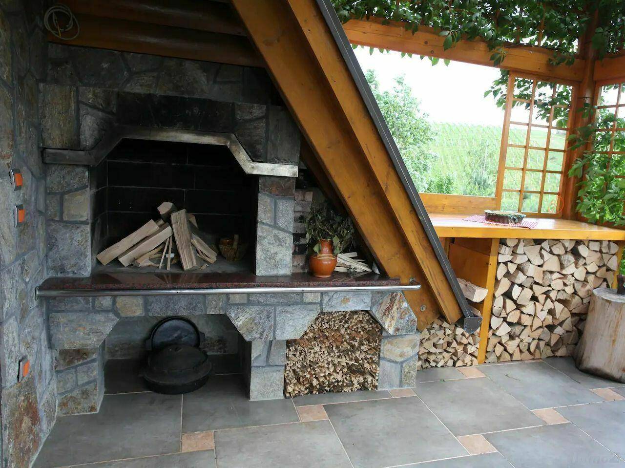 Gemütlicher überdachter Außenbereich mit Steinkamin und Holzvorrat für Grillabende.