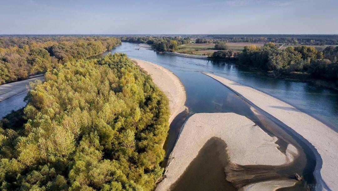Weitläufige Luftaufnahme eines Flusses, der sich durch herbstliche Wälder und Felder unter blauem Himmel windet.
