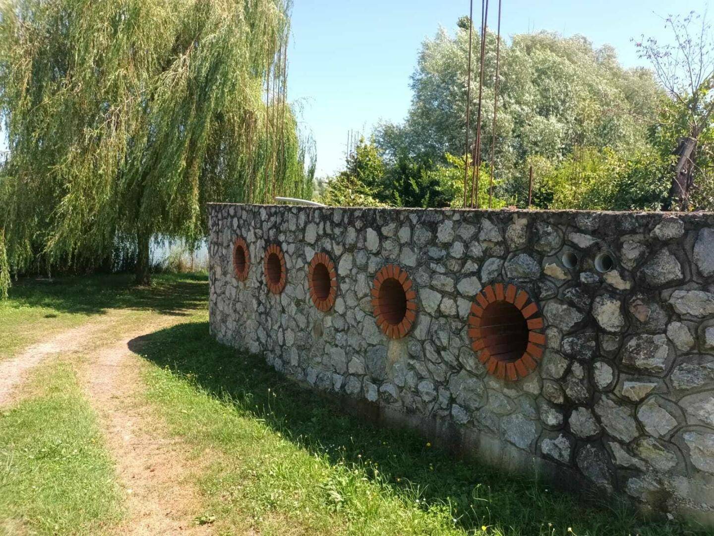 Steinmauer mit dekorativen runden Öffnungen aus Ziegeln, entlang eines grasbewachsenen Pfades.