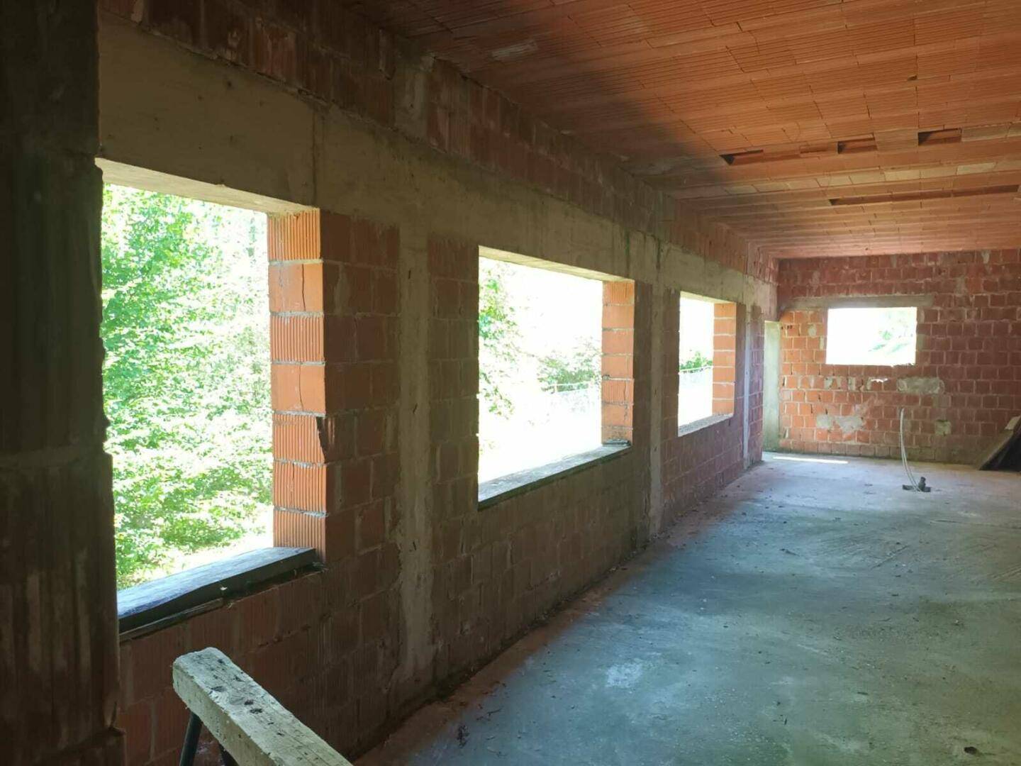 Großer, unfertiger Raum mit unverputzten Ziegelwänden und weitem Blick ins Grüne durch die Fenster.
