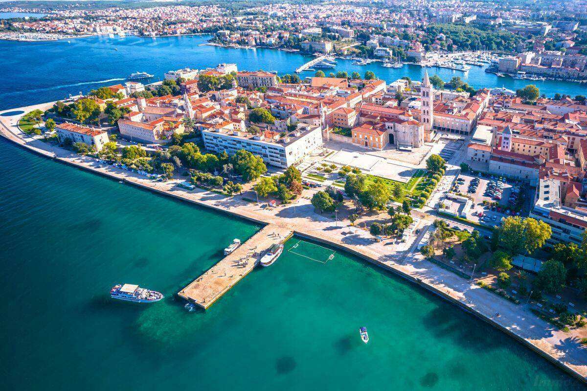 Panoramablick auf eine Küstenstadt mit azurblauem Meer, Hafen und historischen Gebäuden.