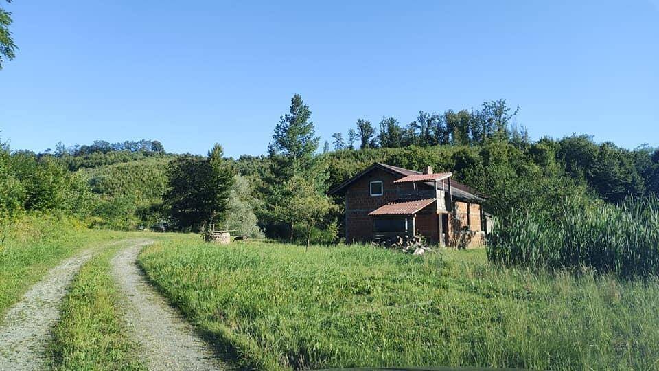 Landhaus in ländlicher Umgebung mit Feldweg, Bäumen und sonnigem Himmel.