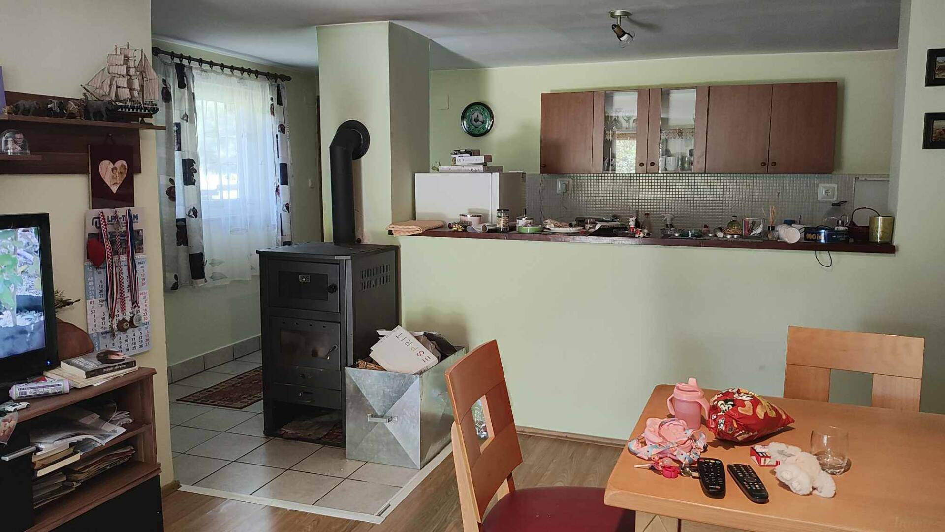 Wohn-Essbereich mit Holzofen, Esstisch und offener Küchenzeile im Hintergrund.