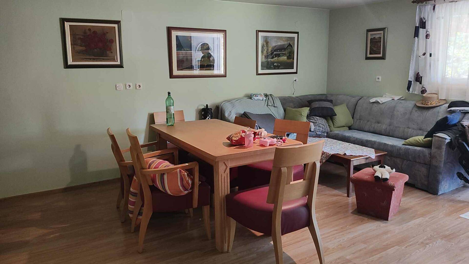 Gemütlicher Wohn-Essbereich mit Esstisch, Sofa und Bildern an hellgrünen Wänden.