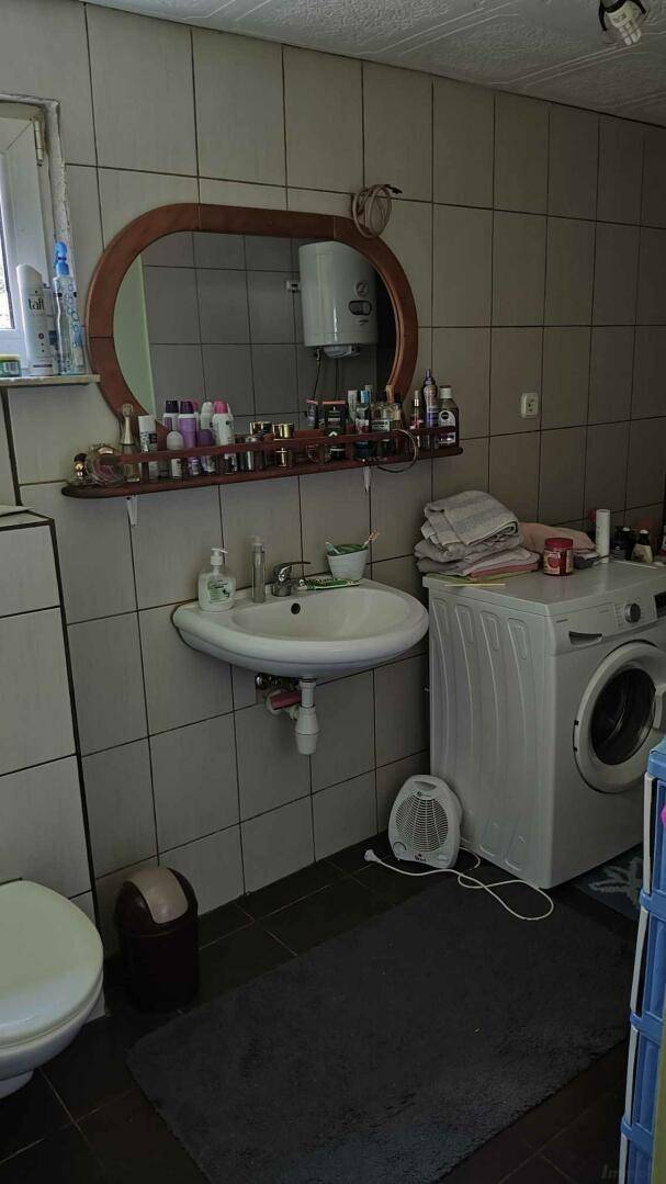 Badezimmer mit Fliesen, Waschbecken, Toilette und Waschmaschine.