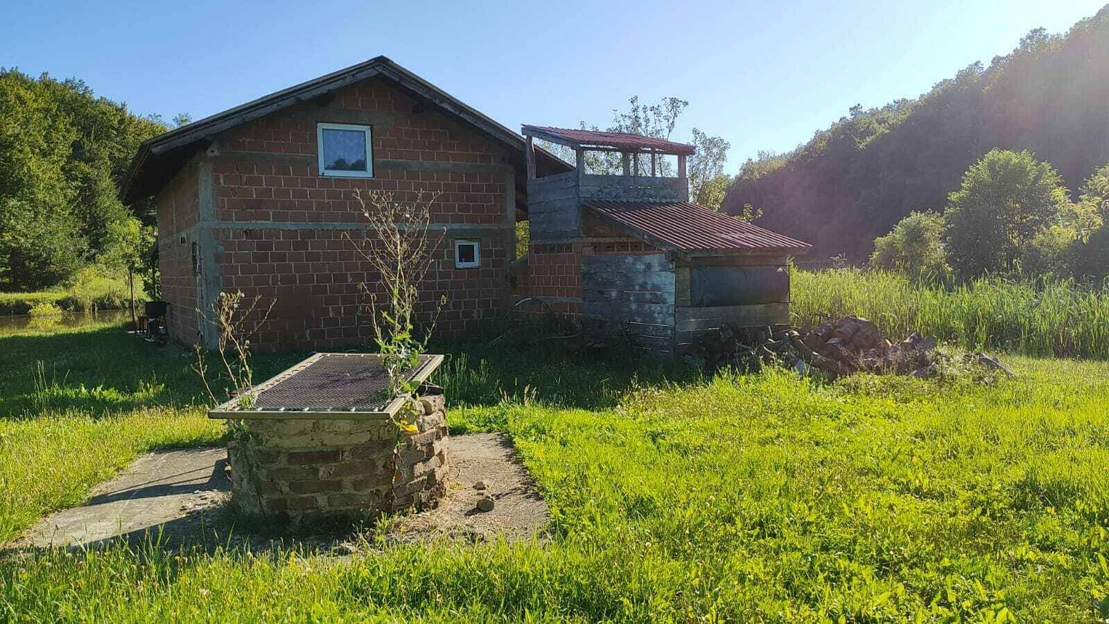 Unfertiges Backsteinhaus am Teich mit ländlicher Umgebung und sonnigem Wetter.