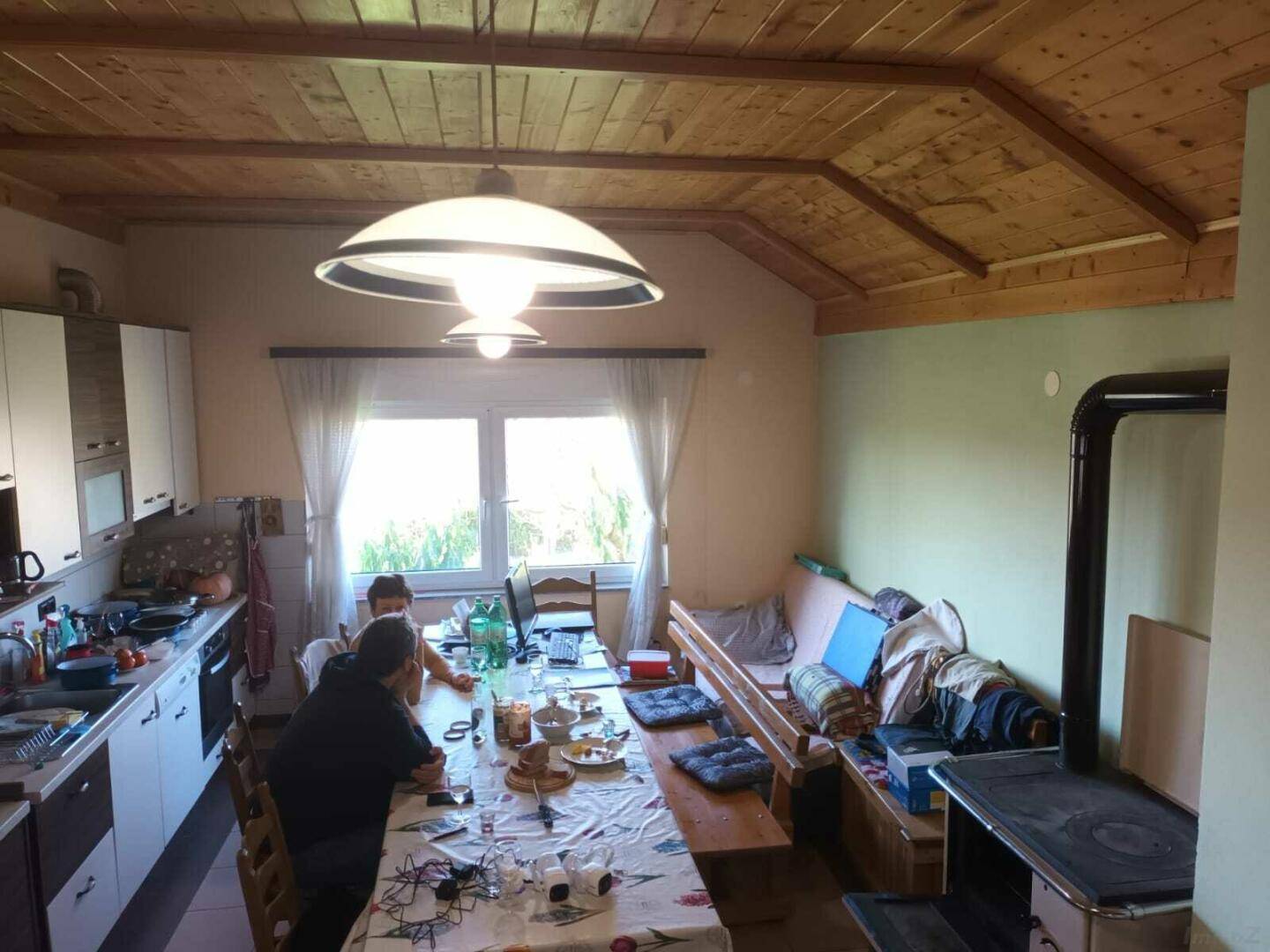 Geräumige Wohnküche mit Holzbalkendecke, Esstisch und traditionellem Ofen.
