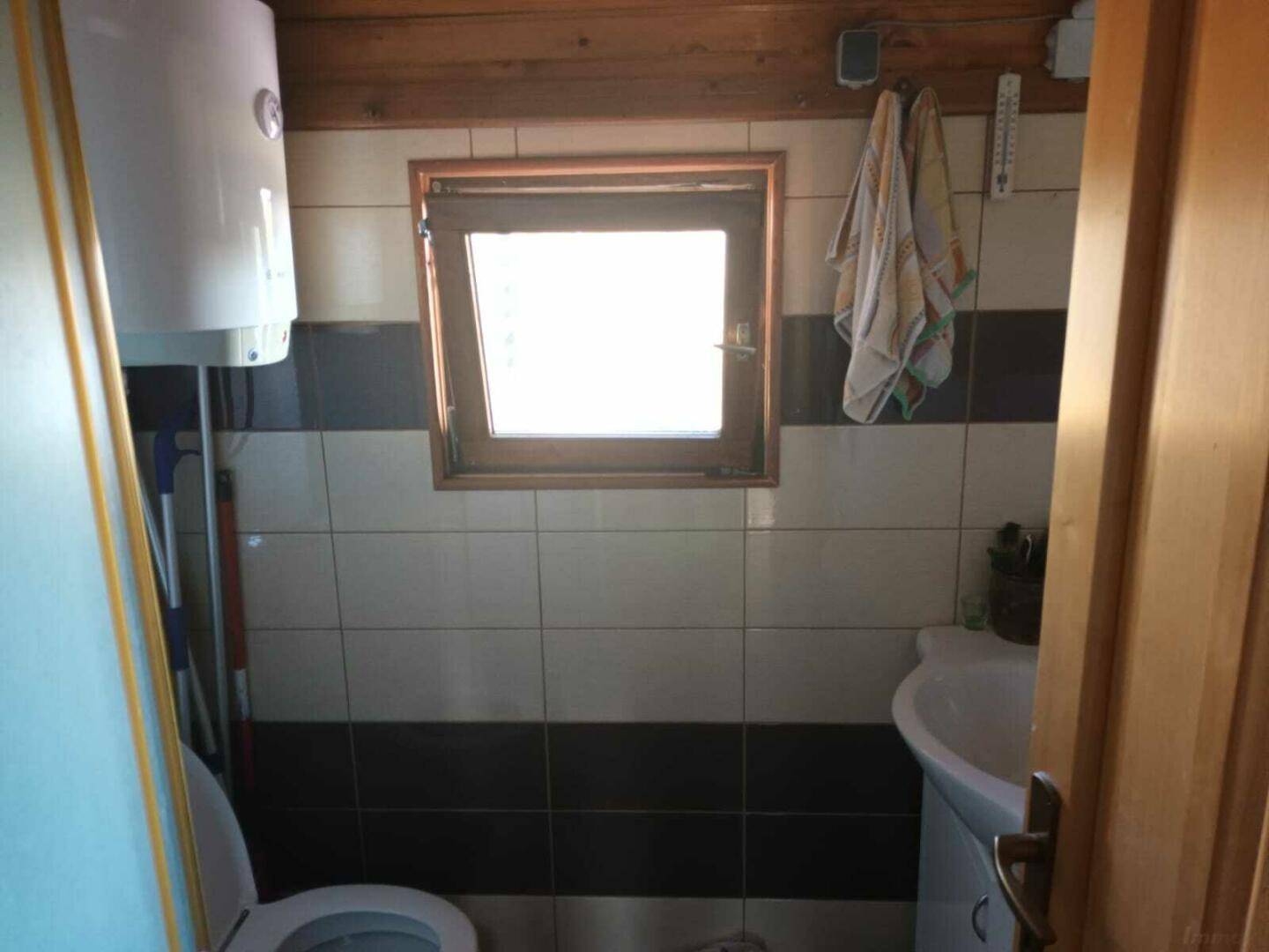 Kleines Badezimmer mit Fliesen in Schwarz-Weiß, Fenster und Warmwasserboiler.