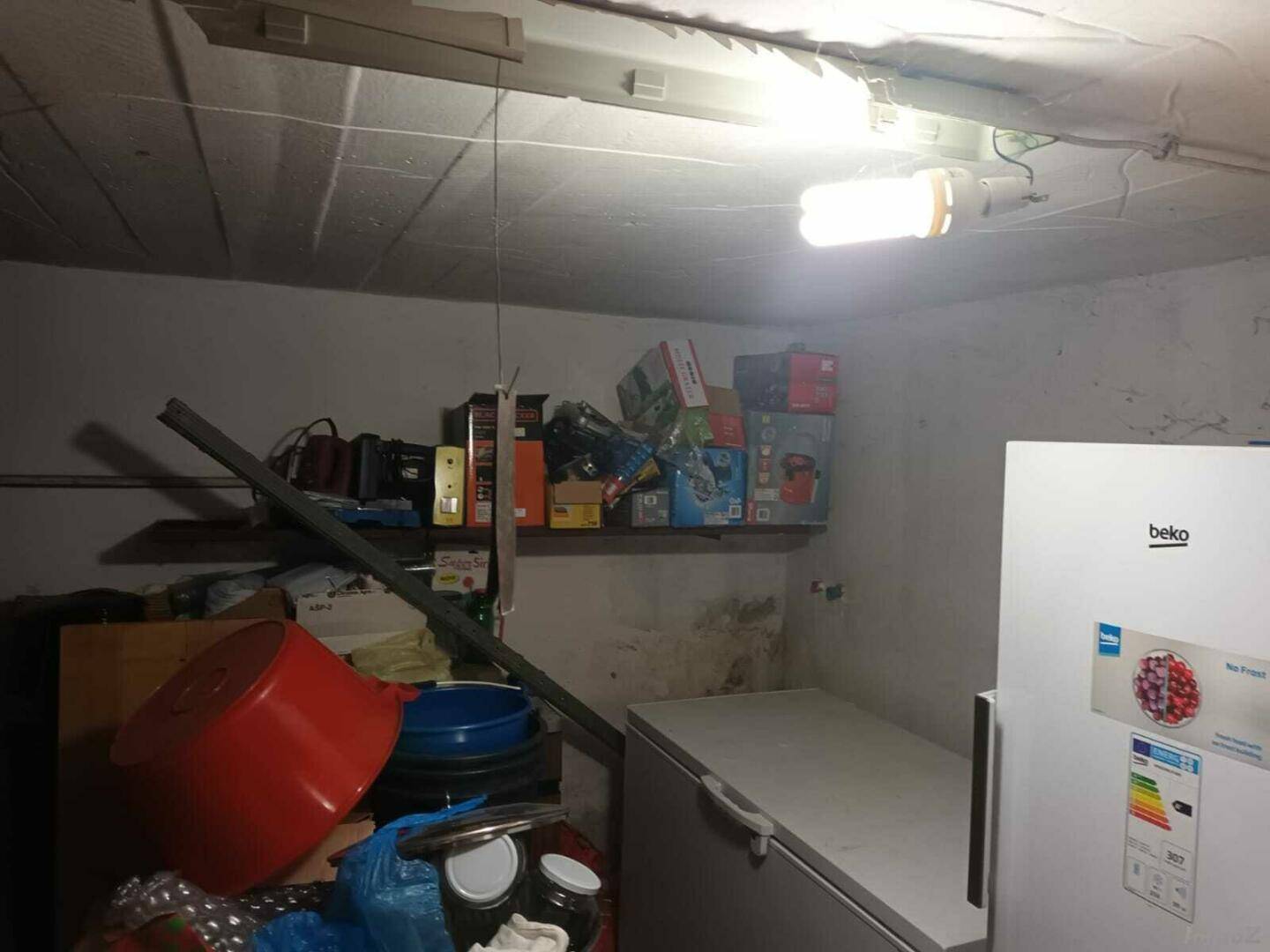 Unaufgeräumter Abstellraum mit Regalen, Kühlschrank und verschiedenen Haushaltsgegenständen.