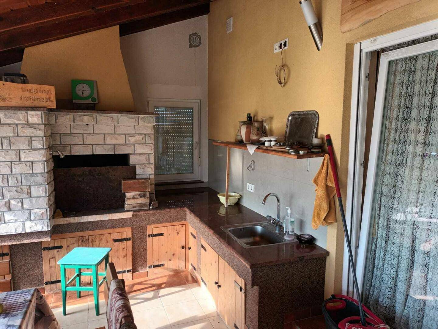 Rustikale Außenküche mit gemauertem Grill, Spüle und Holzelementen unter einer überdachten Terrasse.