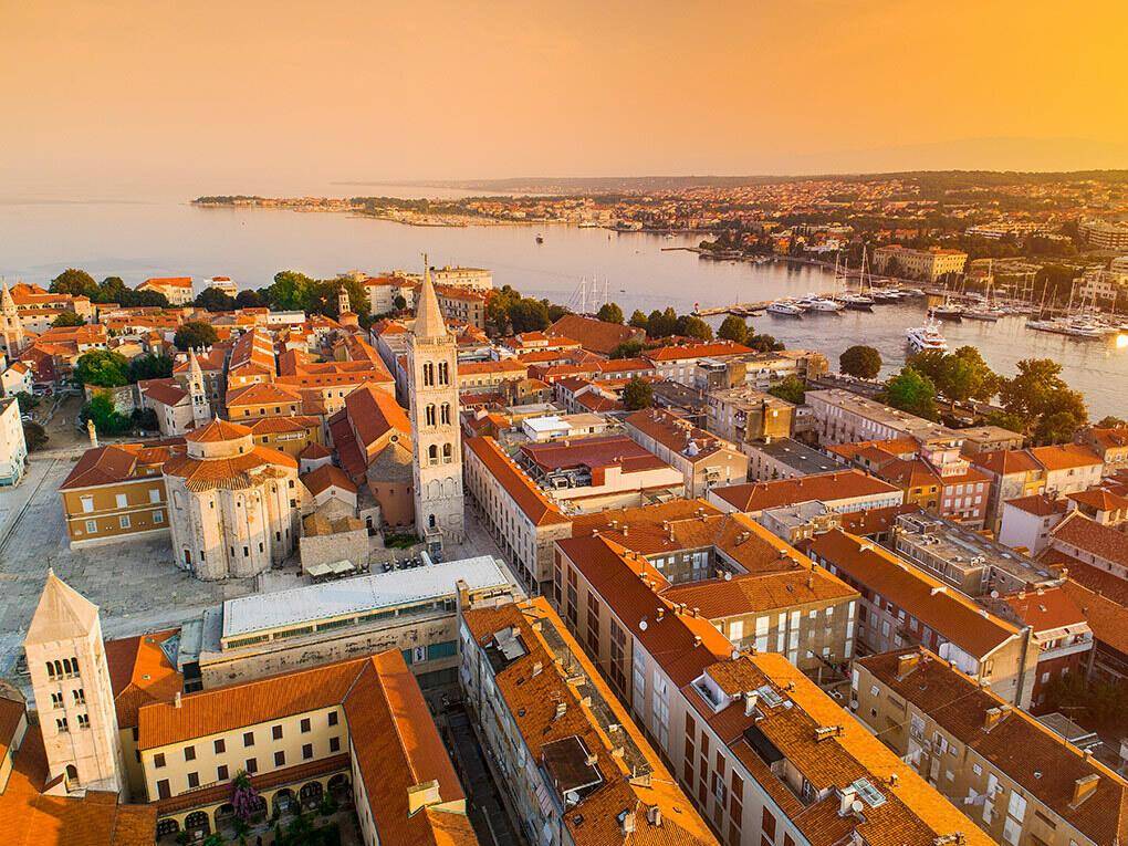 Panoramablick auf eine historische Stadt mit Hafen und zahlreichen Gebäuden bei Sonnenuntergang.