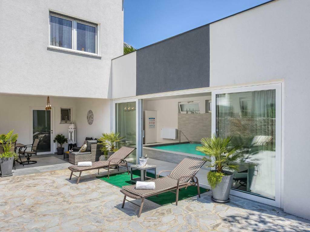 Sonniger Terrassenbereich mit Liegestühlen und Zugang zu einem Innenpool, umgeben von Pflanzen.