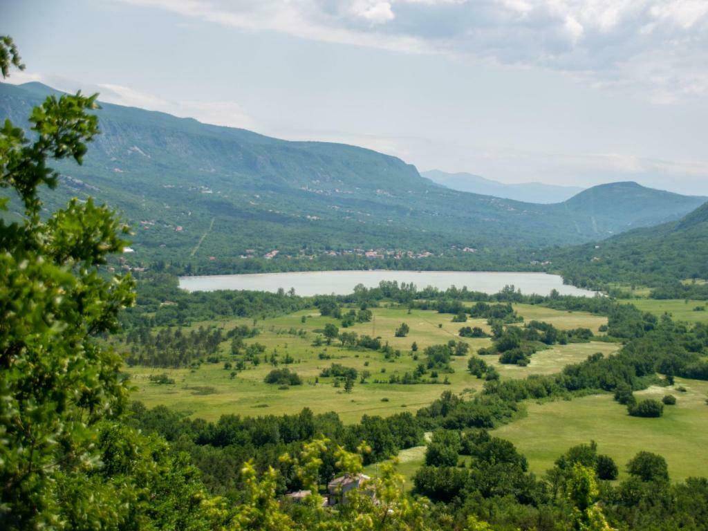 Weitläufiger Blick über ein grünes Tal mit einem See in der Ferne, umgeben von bewaldeten Bergen.