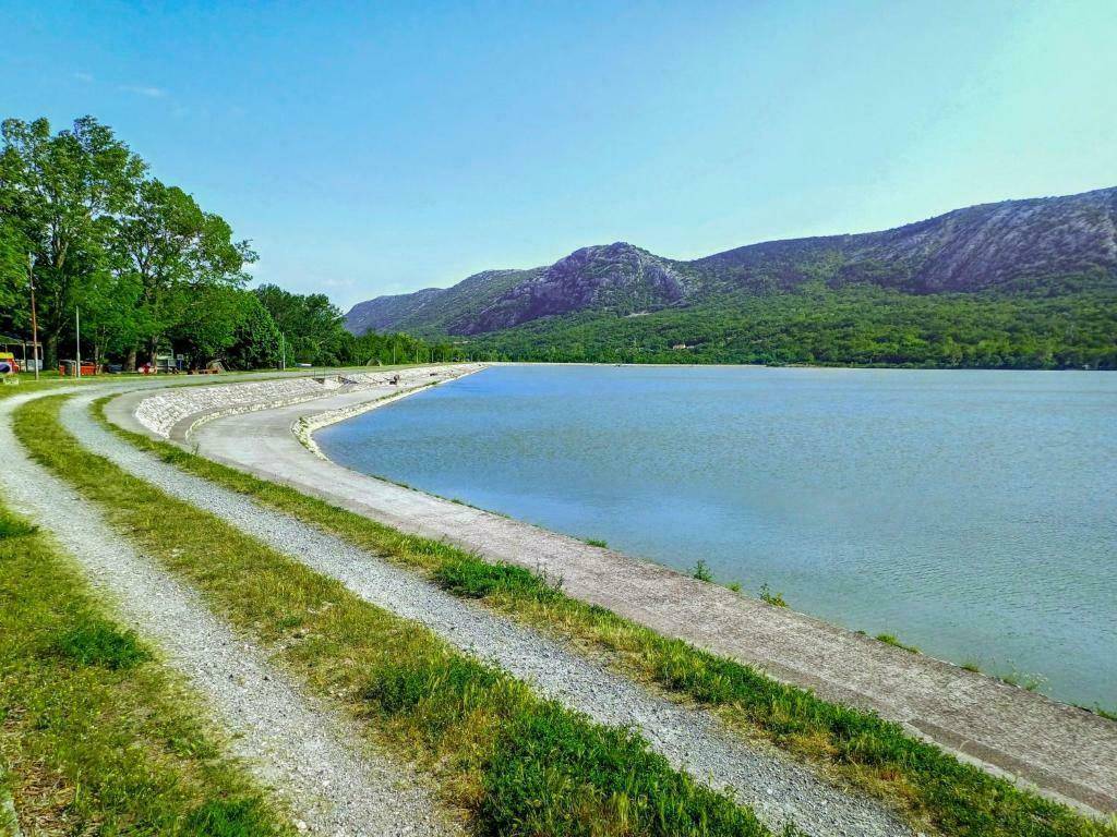 Malerischer See umgeben von grünen Hügeln und Bergen unter einem strahlend blauen Himmel.
