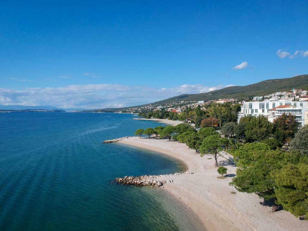 Weitläufiger Küstenabschnitt mit einem ruhigen Strand, umgeben von grünen Bäumen und einer Stadt im Hintergrund.