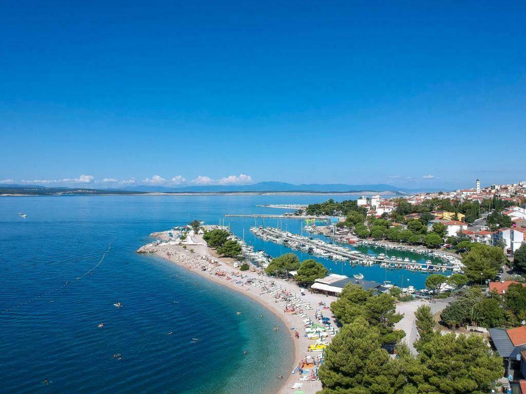 Panoramablick auf eine Küstenstadt mit Yachthafen, Strand und dem weiten blauen Meer unter klarem Himmel.