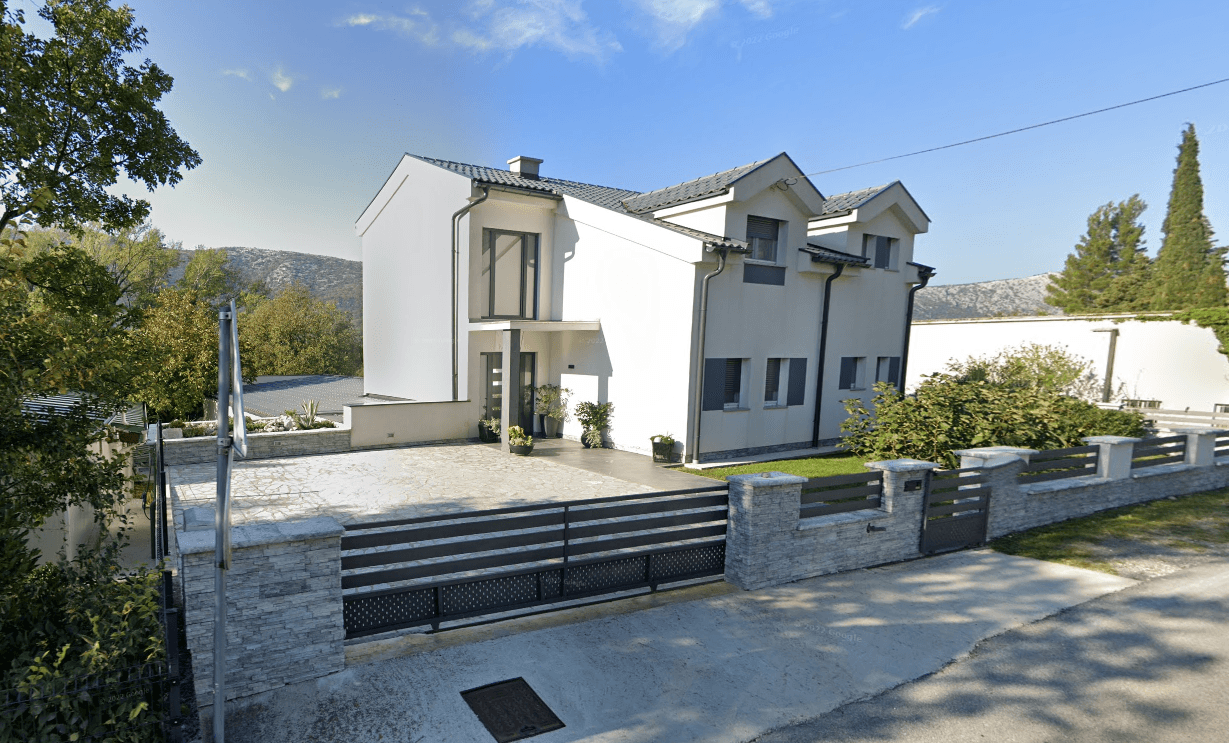 Moderne weiße Hausfassade mit klaren Linien, großen Fenstern und einem gepflegten Vorgartenbereich.