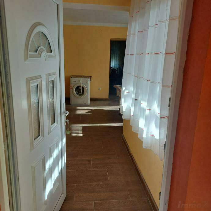 Eingangsbereich mit Fliesenboden, Waschmaschine und hellem Fenster mit Vorhängen.
