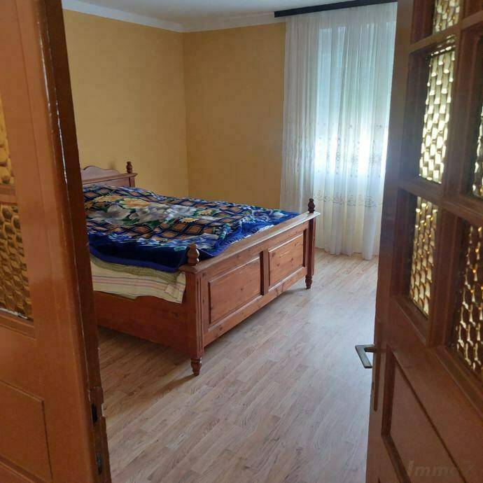 Schlafzimmer mit Holzbett, Laminatboden und hellem Fenster mit Vorhängen.