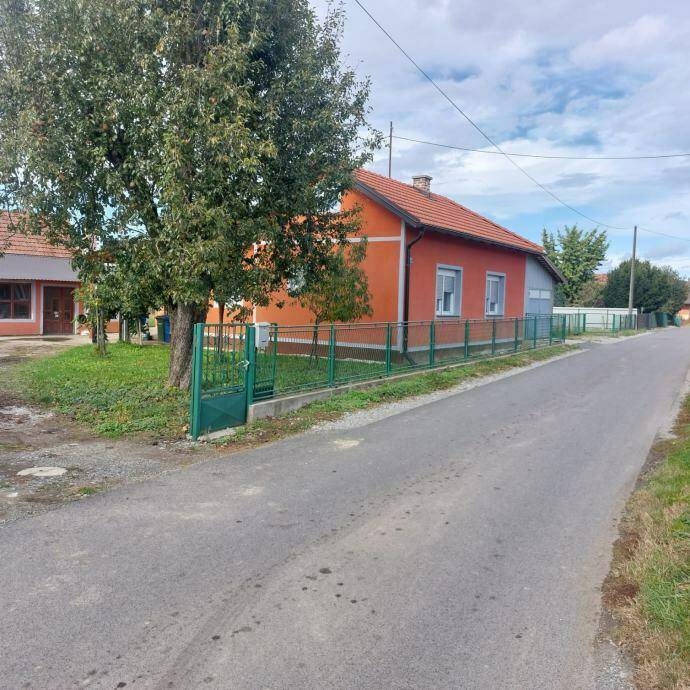 Ansicht des Hauses von der Straße mit grünem Zaun und Bäumen im Vorgarten.