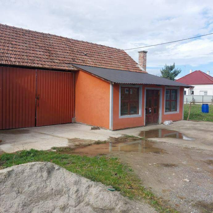 Rückansicht des Hauses mit Garage, gepflastertem Bereich und angrenzendem Grundstück.