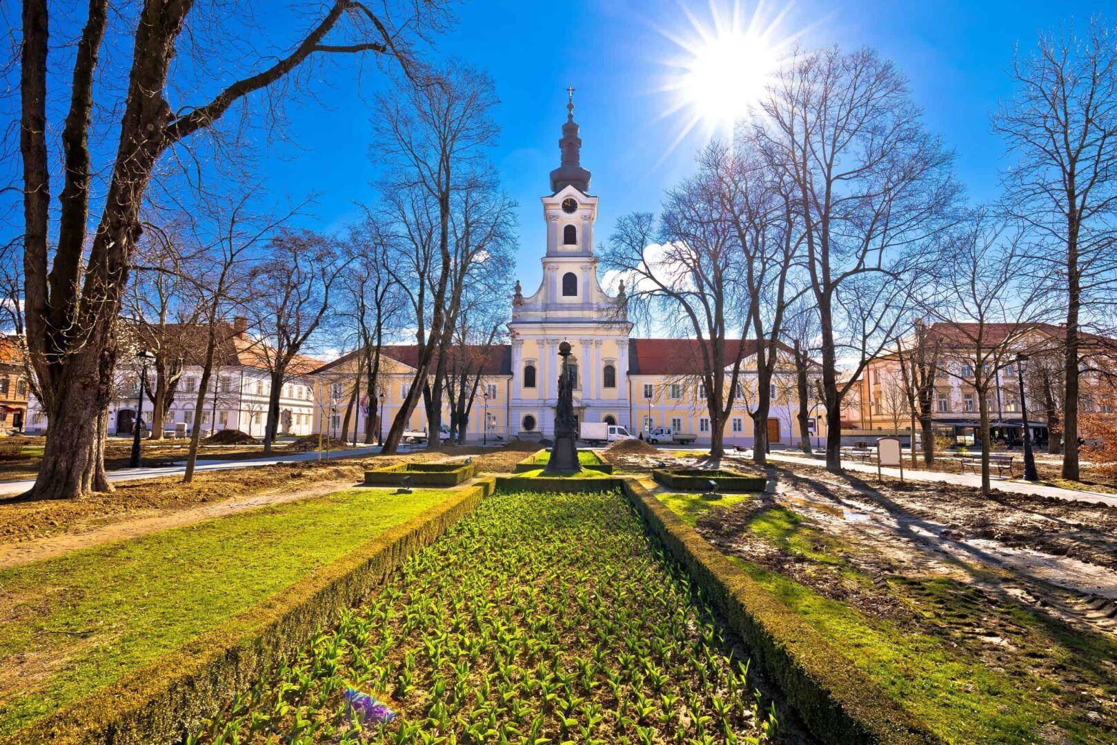 Historisches Gebäude mit markantem Kirchturm und gepflegtem Park unter strahlend blauem Himmel.