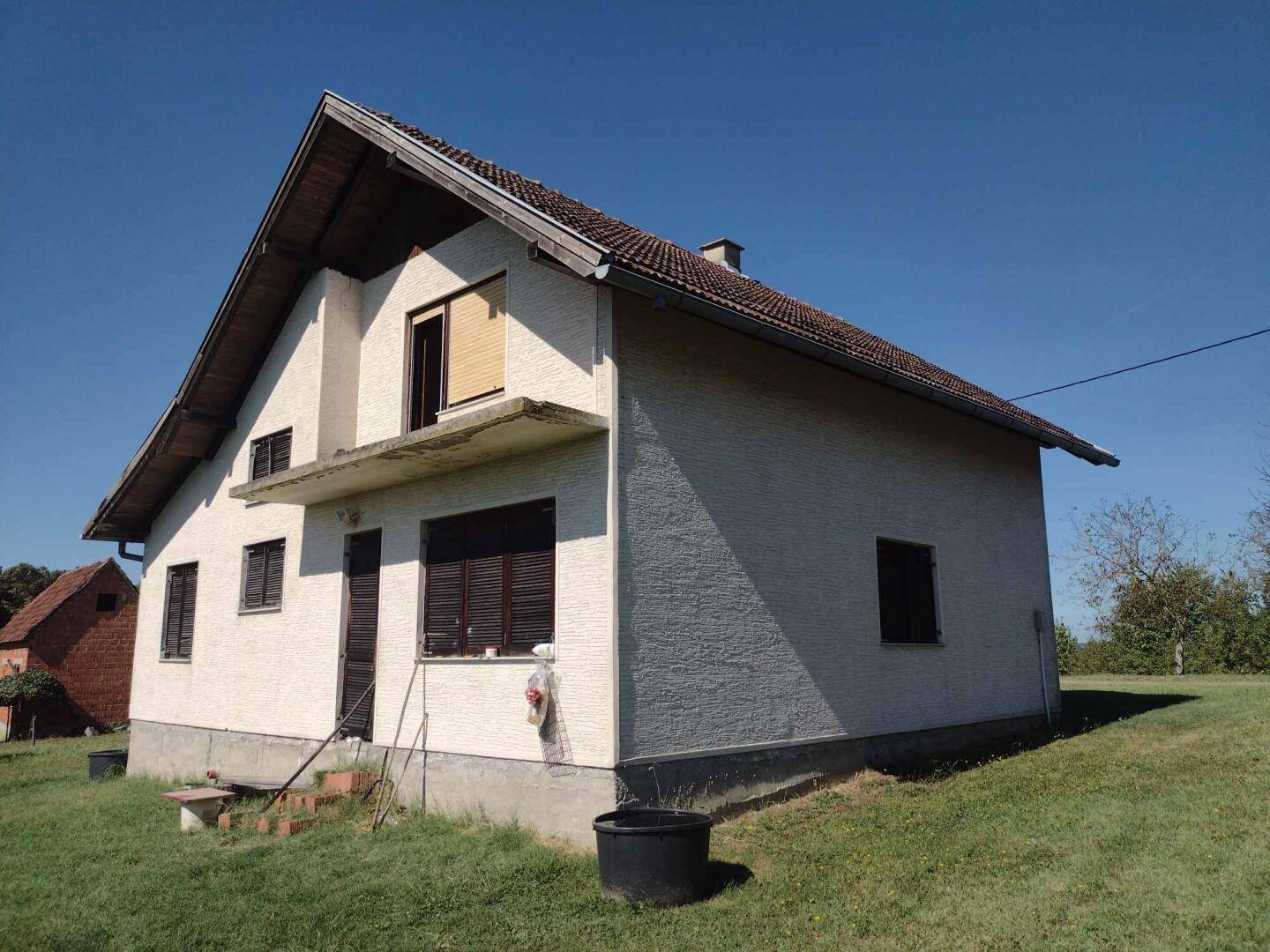 Einfaches Wohnhaus mit heller Fassade, Satteldach und Fensterläden, umgeben von einer grünen Wiese.