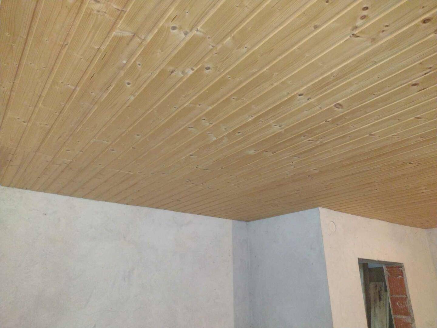 Innenraum mit einer Decke aus Holzpaneelen und unverputzten Wänden, die auf eine Renovierung warten.
