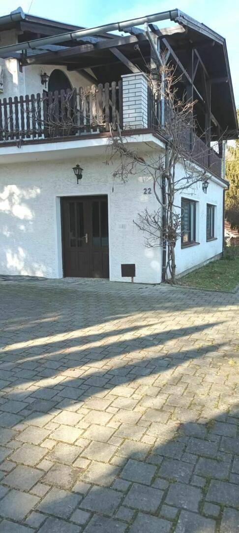 Seitenansicht des Hauses mit gepflasterter Einfahrt, Balkon und umgebender Natur.