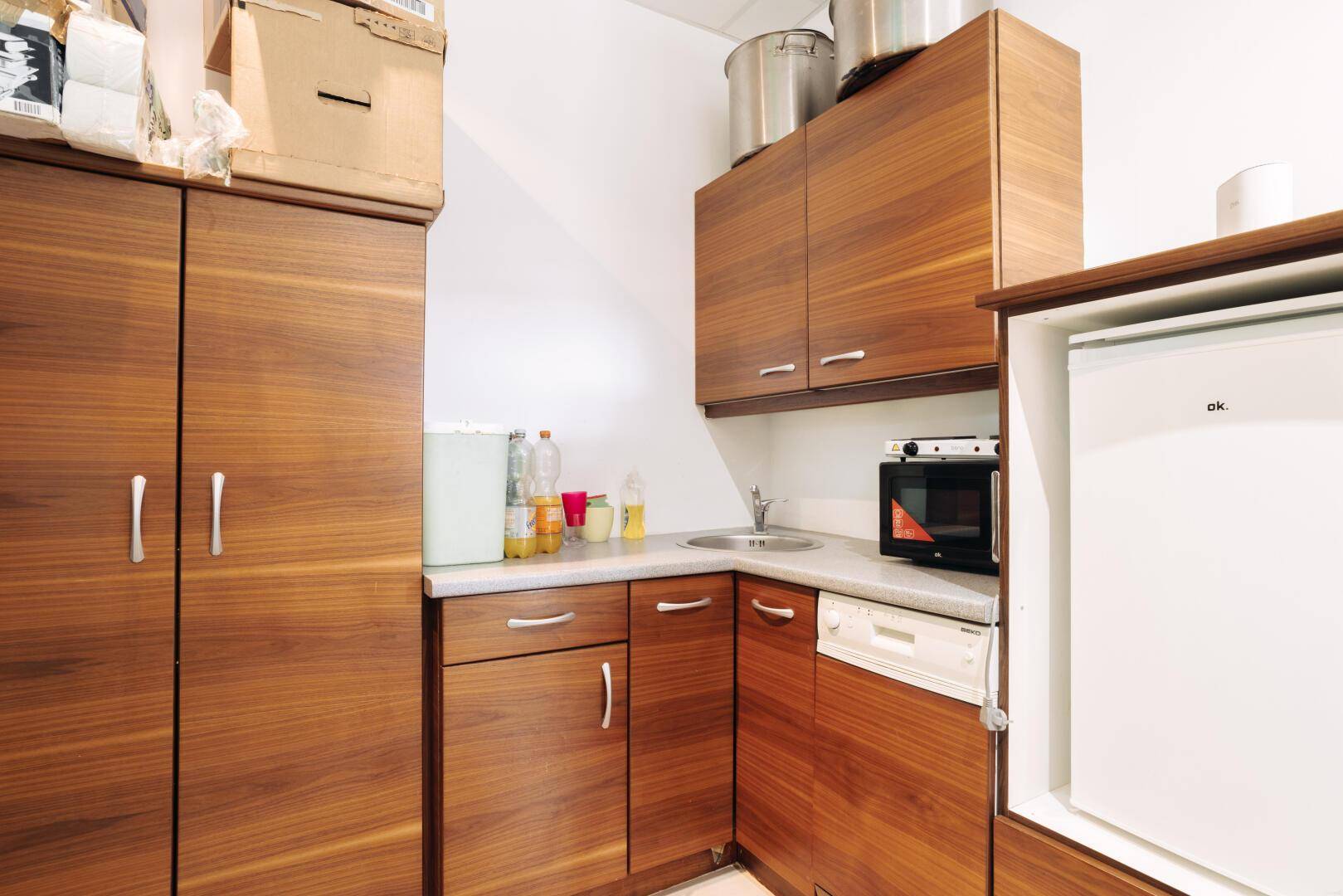 Kompakte Küchenzeile mit Holzschränken, Spüle, Mikrowelle und Kühlschrank.