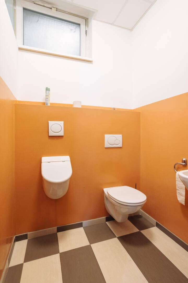 Modernes WC mit orangefarbenen Wänden, Fenster und schwarz-weiß kariertem Fliesenboden.