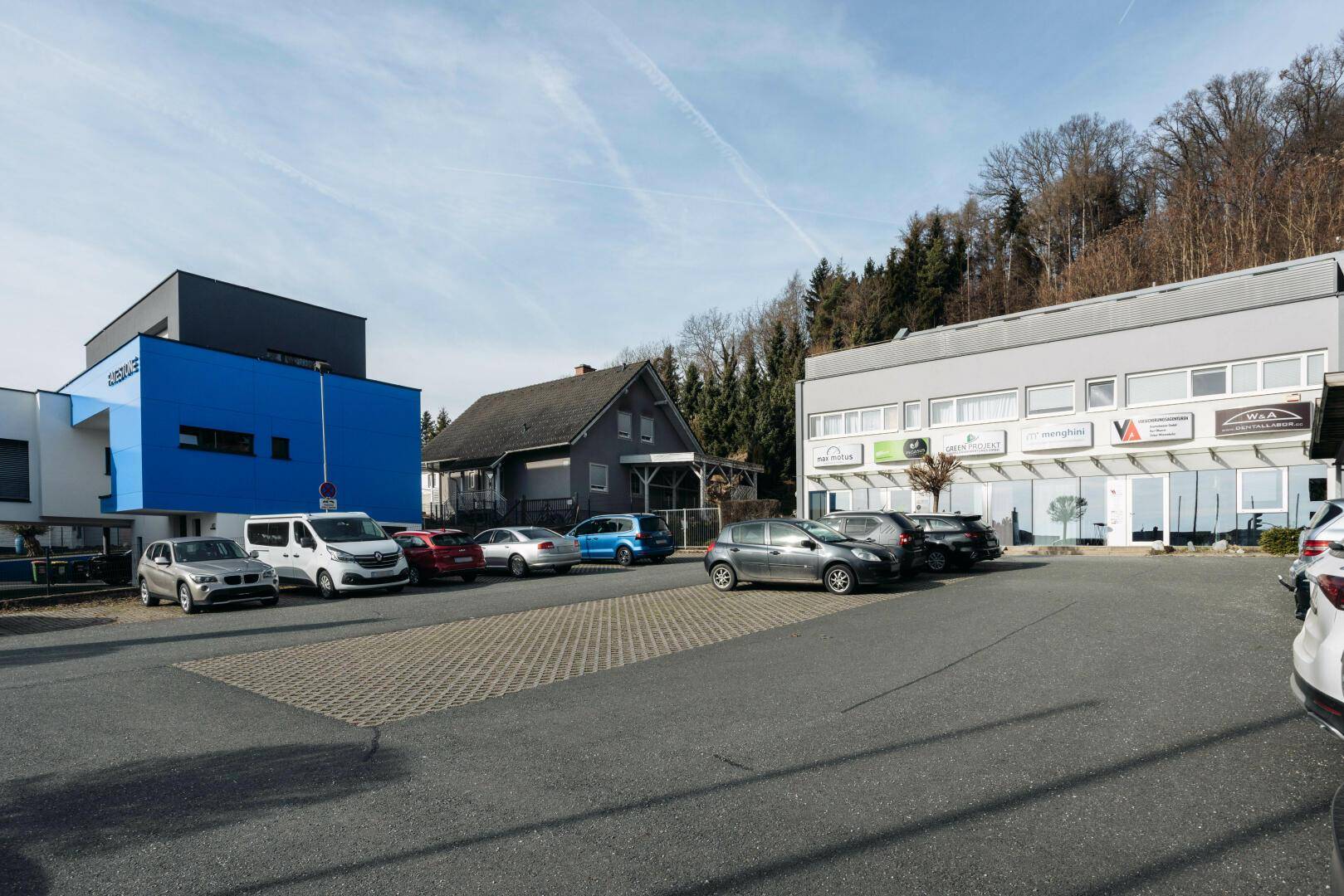 Mehrere Geschäftsgebäude mit Parkplätzen und umliegender Natur unter blauem Himmel.
