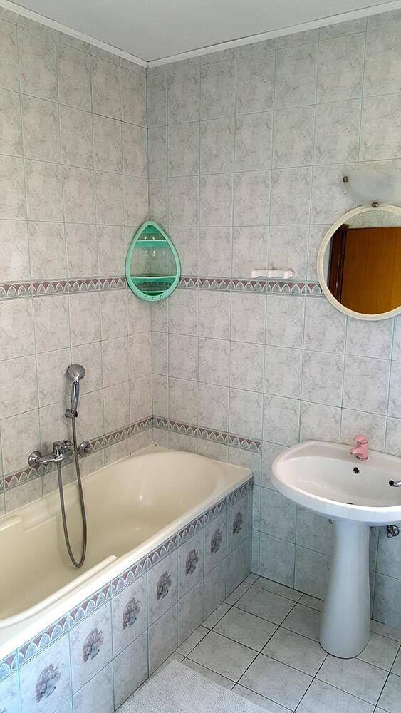 Badezimmer mit Badewanne, Waschbecken und hellen Fliesen an Wänden und Boden.