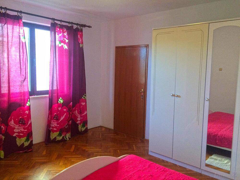 Schlafzimmer mit Parkettboden, weißem Kleiderschrank und farbenfrohen Vorhängen.