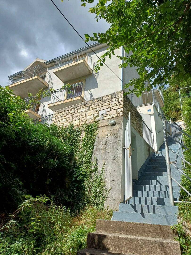 Außenansicht des Gebäudes mit mehreren Balkonen und einer Steintreppe, umgeben von Vegetation.