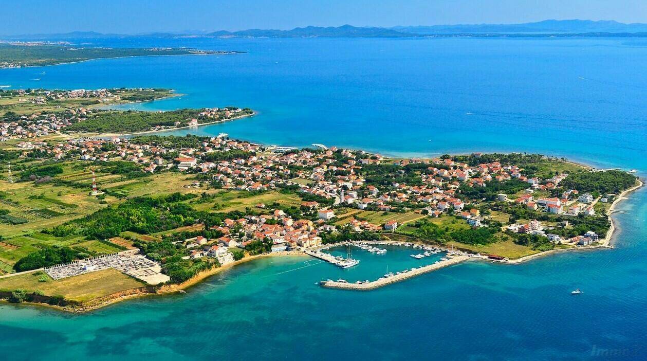 Luftaufnahme einer Küstenstadt mit Hafen und umliegender Landschaft am Meer.