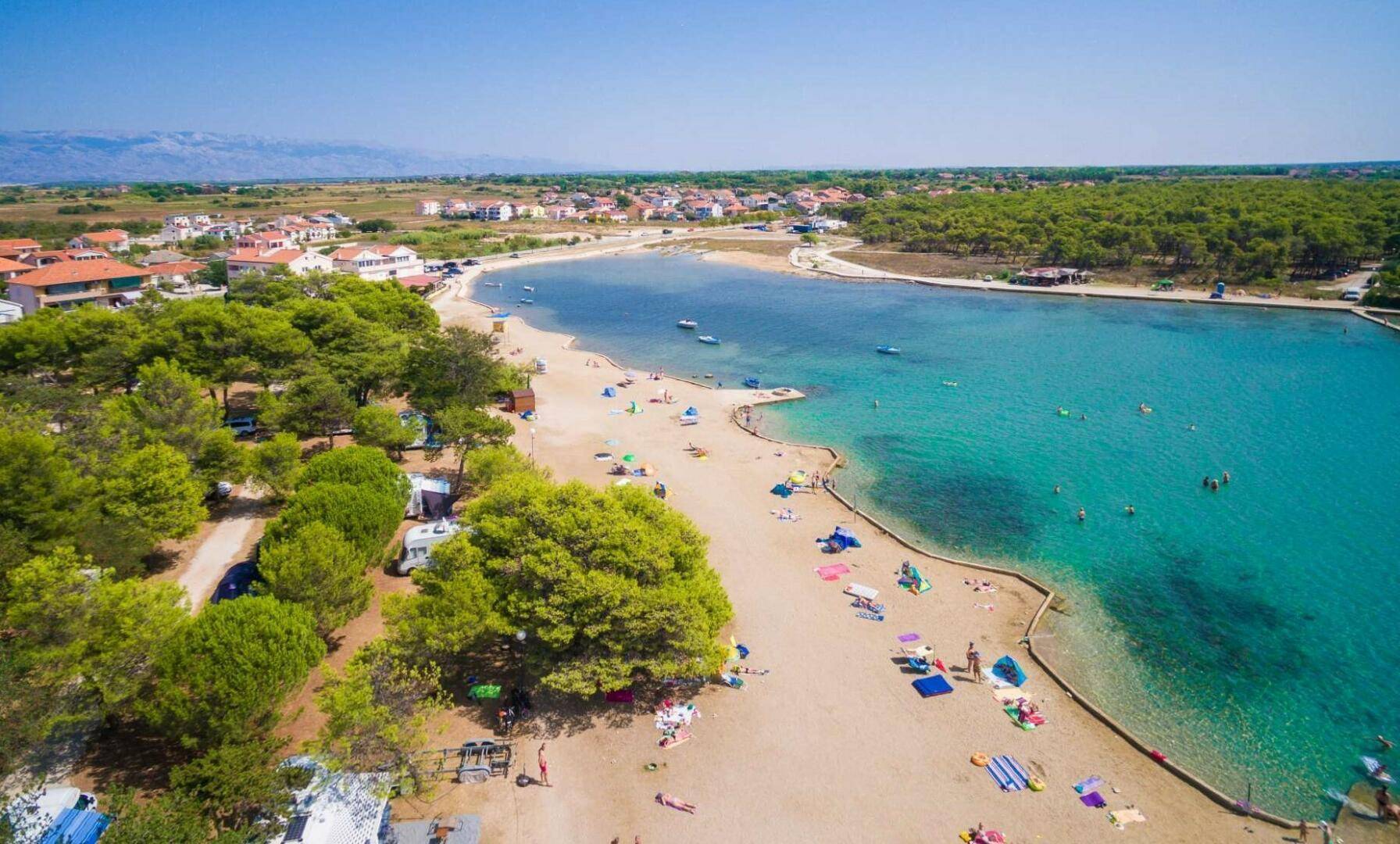 Belebtes Strandgebiet mit klarem türkisfarbenem Wasser, vielen Badegästen und grüner Umgebung.